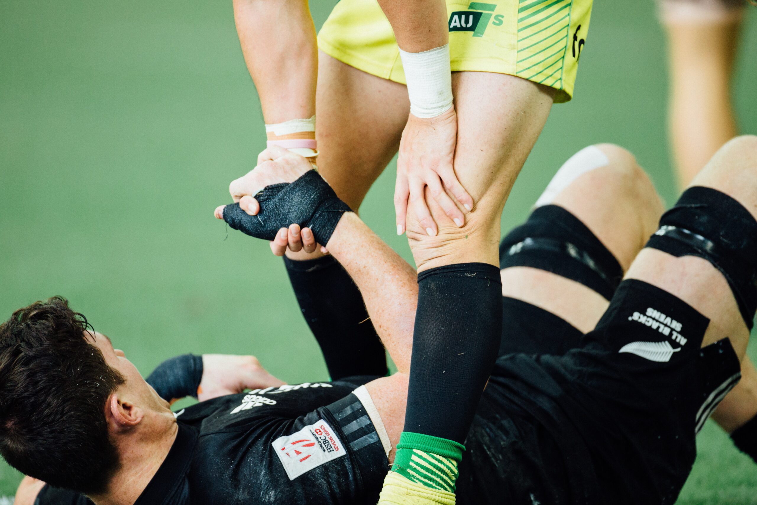 Picture of two soccer players, one is lying down and the other is helping him up with a hand on his knee to suggest there is ACL rehabilitation underway
