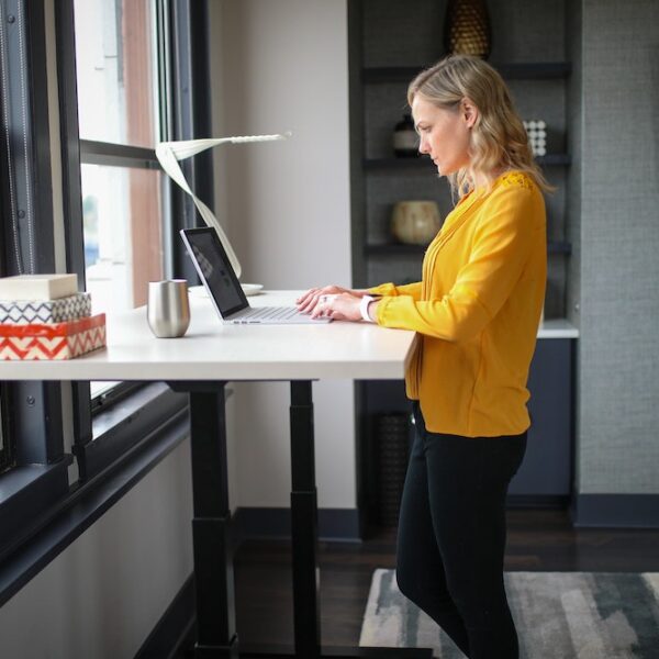 Picture of a woman at a standing desk looking at a screen with an office environment in the background