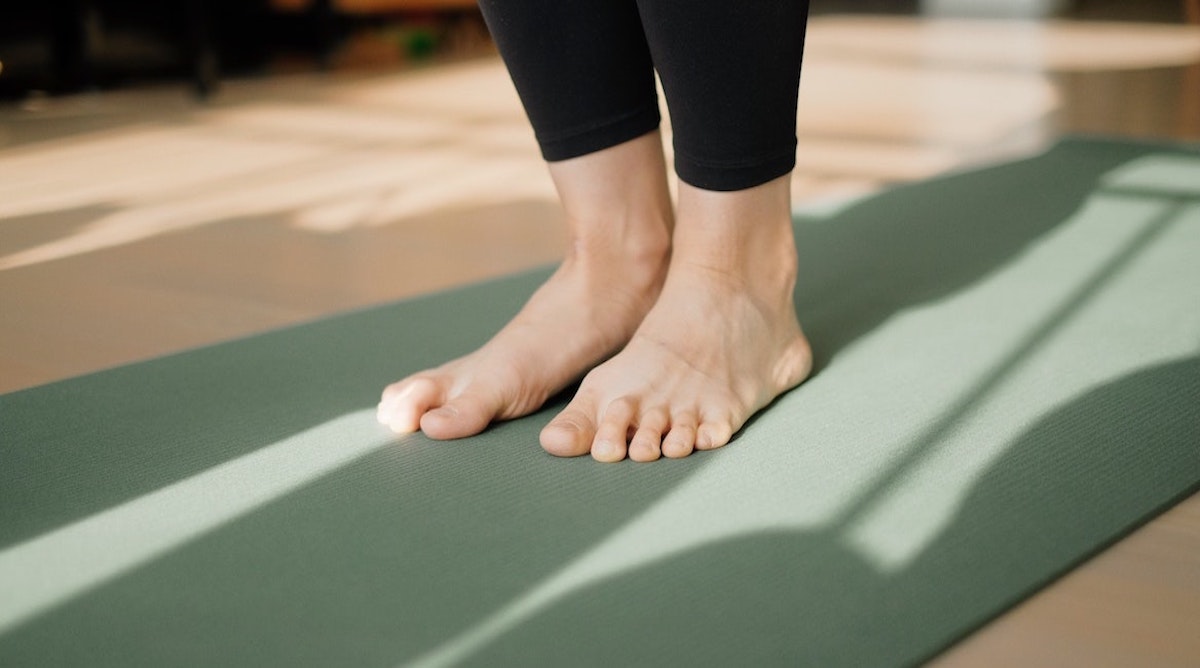 Picture of a woman standing on a green reformer mat wearing pilates pants