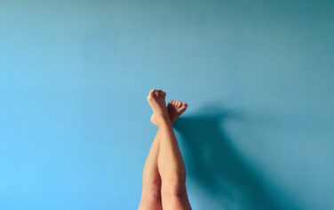 Picture of a women's feet held up in the air against a blue background, symbolising podiatry health from Bared Footwear