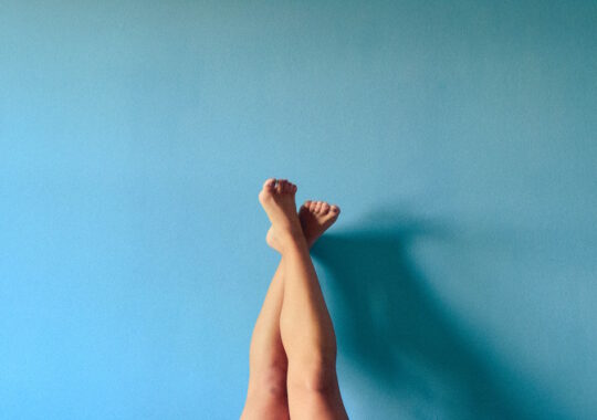 Picture of a women's feet held up in the air against a blue background, symbolising podiatry health from Bared Footwear