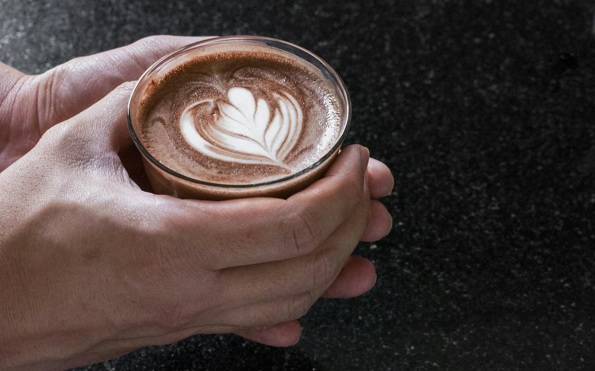 Picture of a person holding a dairy free hot chocolate with a milk pattern